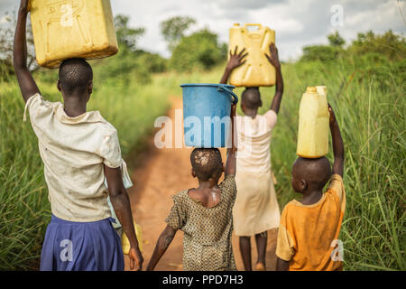 Gruppe, wenn junge afrikanische Kinder wandern mit Eimer und Kanister auf den Kopf, wie sie sich vorbereiten, sauberes Wasser zurück in ihr Dorf zu bringen. Stockfoto