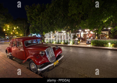 Alte Citroen Traction Avant, beleuchtet die französische Kolonialzeit Gebäude und Laternen hängen in den Bäumen auf idyllischen Sakkaline Straße in Luang Prabang, Laos, in der Dämmerung. Stockfoto