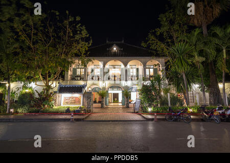 Paar Roller vor der beleuchteten Villa Santi, ein Hotel in einer alten französischen Kolonialzeit Gebäude auf einer idyllischen Sakkaline Straße in Luang Prabang, Laos, in der Dämmerung. Stockfoto