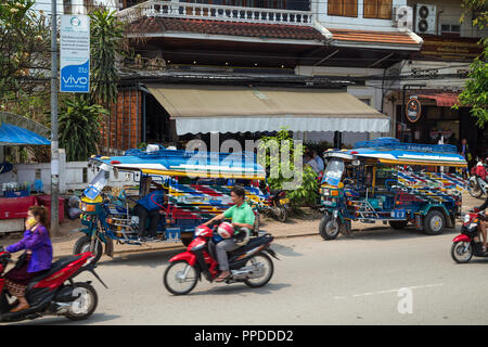 Roller und zwei geparkte farbenfrohe Dreirad Taxi genannt Jumbo (oder Tuk Tuk) auf dem Sisavangvong Straße in Luang Prabang, Laos, an einem sonnigen Tag. Stockfoto