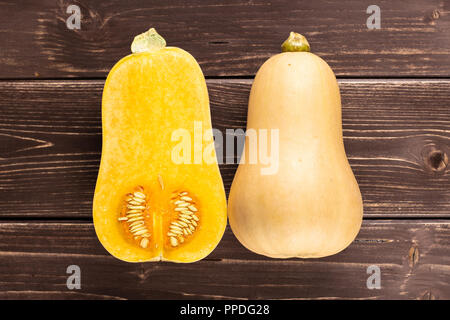 Eine ganze Hälfte von glatten Birnenförmig orange Kürbis waltham Vielzahl flatlay auf braunem Holz Stockfoto