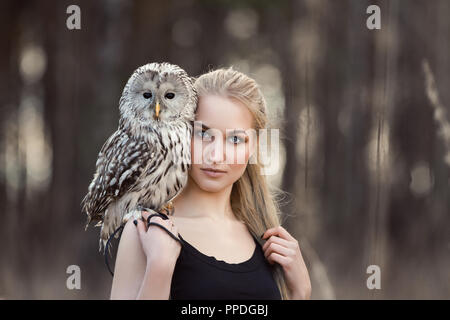 Frau blond im Herbst im Pelzmantel mit Eule an Hand der erste Schnee. Schöne Mädchen mit langen Haaren in der Natur, eine Eule. Romantisch, zarten look Mädchen Stockfoto