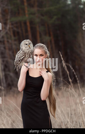 Frau blond im Herbst im Pelzmantel mit Eule an Hand der erste Schnee. Schöne Mädchen mit langen Haaren in der Natur, eine Eule. Romantisch, zarten look Mädchen Stockfoto
