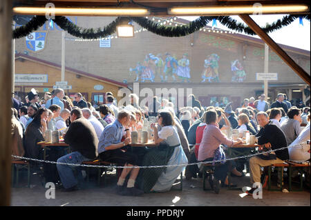 Besucher sitzen draußen in der Sonne auf dem Oktoberfest. Stockfoto