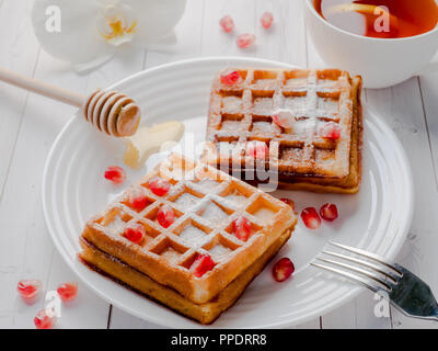 Lecker köstliche Wiener Waffeln mit Honig und Granatapfel Samen auf eine weiße Platte, hellen Hintergrund. Stockfoto