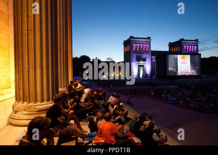 Die Zuschauer sitzen auf der Treppe von der Staatlichen Antikensammlungen (staatliche Sammlungen von Antiquitäten) im Kino Open Air am Königsplatz in München. Stockfoto