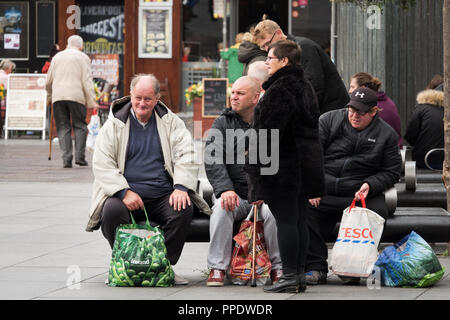 Drei Männer, die ein Tesco, Aldi und Island Tragetaschen setzen sie sich für eine Pause vom Einkaufen im Stadtzentrum von Liverpool. Stockfoto