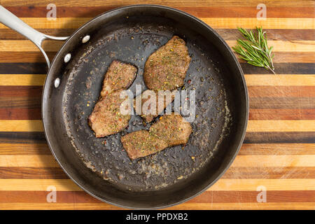 Schwarze Pfanne mit gebratenem Rumpsteak Neben grüne Kräuter über gestreifte Holz- Hintergrund Stockfoto