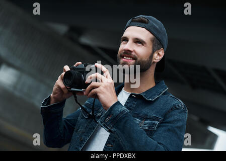 Fotografie Hobby. Junge stilvollen Mann auf der Straße der Stadt, die Fotos auf der Kamera freuen uns lächelnd freudige close-up Stockfoto