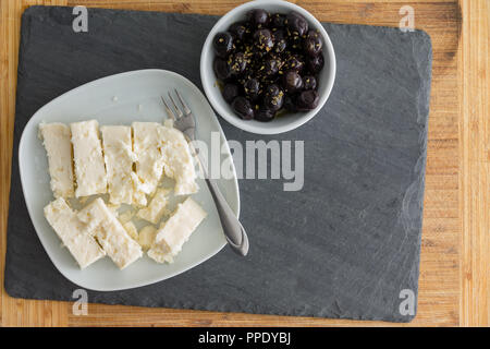 Servieren von frischen schwarzen gewürzten Mediterranen Oliven und leckere griechische Feta Käse in den einzelnen Schalen auf einem schwarzen Schiefer Brett über Holz von abov gesehen Stockfoto