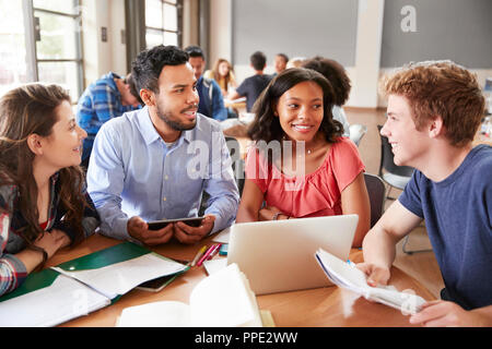 Schülerinnen und Schüler mit Laptops und digitale Tabletten Arbeiten mit männlichen Lehrer am Schreibtisch Stockfoto