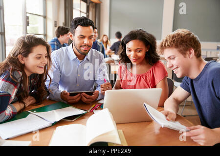 Schülerinnen und Schüler mit Laptops und digitale Tabletten Arbeiten mit männlichen Lehrer am Schreibtisch Stockfoto