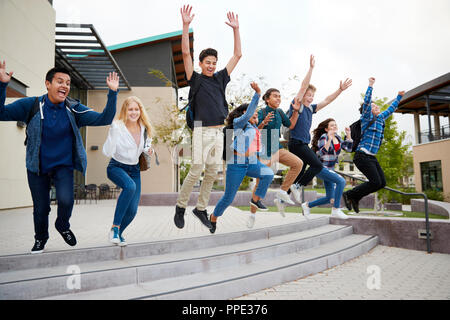 Gruppe von Schülern das Springen in die Luft außerhalb der Hochschule Gebäude Stockfoto