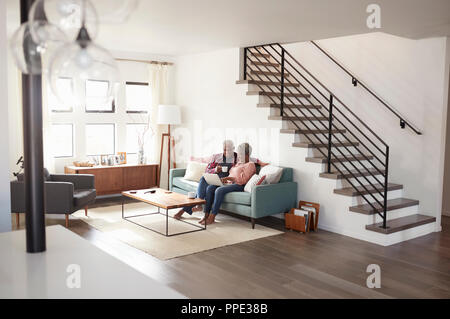 Senior Paar sitzt auf einem Sofa zu Hause mit Laptop Online Zu Kaufen Stockfoto