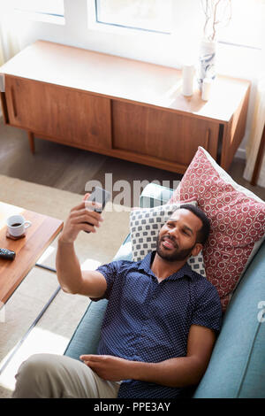 Draufsicht des Menschen liegend auf dem Sofa zu Hause Posieren für Selfie auf Handy Stockfoto