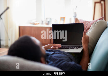 Mann, liegend auf dem Sofa zu Hause mit Laptop Stockfoto