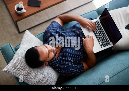 Draufsicht des Menschen liegend auf dem Sofa zu Hause mit Laptop Stockfoto