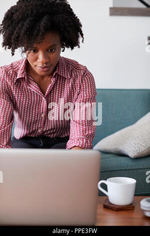Frau sitzt auf einem Sofa zu Hause mit Laptop Stockfoto