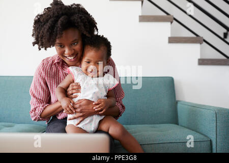 Mutter mit Baby Tochter sitzt auf einem Sofa zu Hause auf Laptop Stockfoto