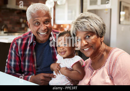 Portrait der Großeltern mit Baby Enkelin um den Tisch zu Hause sitzen Stockfoto