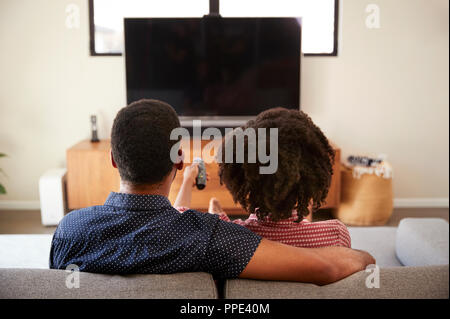 Rückansicht des Paares auf Sofa vor dem Fernseher zusammen sitzen Stockfoto
