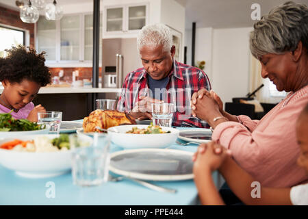 Großeltern Beten vor dem Essen zu Hause mit Enkelinnen Stockfoto