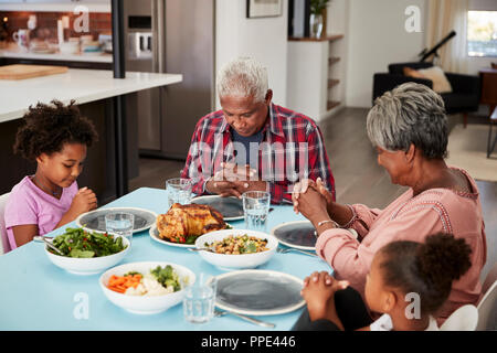 Großeltern Beten vor dem Essen zu Hause mit Enkelinnen Stockfoto