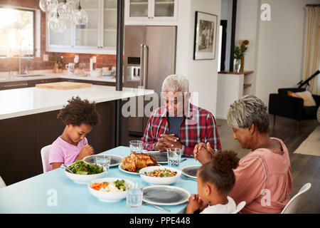 Großeltern Beten vor dem Essen zu Hause mit Enkelinnen Stockfoto