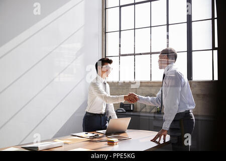 Zwei Geschäftsleute stehen die Hände schütteln über Schreibtisch in einem Büro Stockfoto