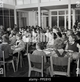 1950, historische, Grundschule Kinder zusammen an der hölzernen Tischen ihre Schule Abendessen (Mittagessen), England, Grossbritannien in sitzen. Stockfoto