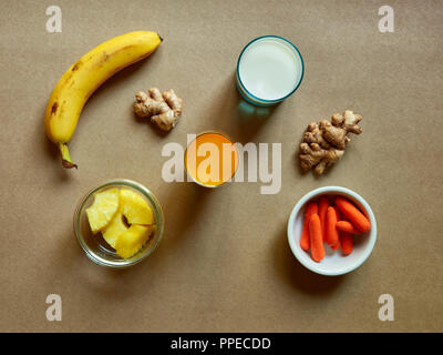 Oben Blick auf ein Glas Saft mit frischen Karotten und Ingwer smoothie Zutaten über braunen Hintergrund im Studio. Stockfoto
