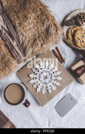 Winter gemütliche Konzept. Pelz, Plaid, Notebook, Tasse Kaffee, Kekse, Schokolade Süßigkeiten auf dem Bett Weihnachtskarte mockup Kopie Raum Stockfoto