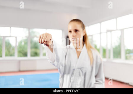 In der Nähe von Frau Faust werfen Punch gegen die grossen Fenster im Kampf Klasse. Auf unscharfen Hintergrund Kämpferin mit blauen Augen und geflochtene Haare ernsthaft gerade mit geballter Faust. Konzept der Sport. Stockfoto