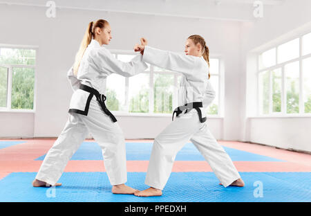 Zwei junge sportliche Mädchen kämpfen mit Techniken in der leichten Klasse Karate Karate. Starke Frauen, die in den weißen Kimono und schwarze Riemen, Wettbewerbe unter sich. Konzept der Sport. Stockfoto