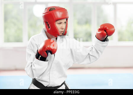 Kämpferin Durchführung kick Verbesserung der Technik der Kampf. Hübsche junge Frau in Angriff Position tragen in der Kampfkunst einheitliche und rote Handschuhe und Helm mit Schuhe für den Kampf im Fitnessstudio. Stockfoto