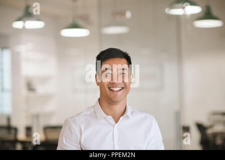 Junge asiatische Geschäftsmann lachend, während in einem modernen Büro stehend Stockfoto