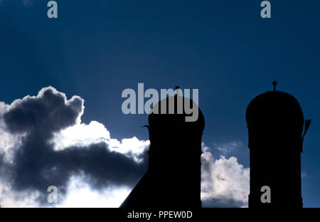 Silhouette der beiden Türme der Frauenkirche in München, in der vor einem dramatischen bewölkten Himmel und Sonne. Stockfoto