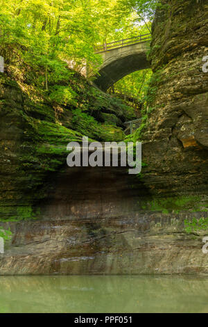 Eine Fußgängerbrücke über eine kleine Schlucht mit einem ausgetrockneten Wasserfall. Stockfoto