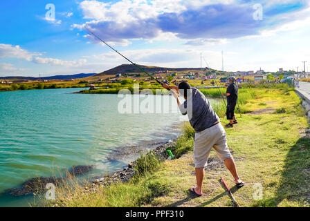 Temelli, Ankara/Türkei - am 10. August 2018: fiser Mann weg wirft seine Angel gegen den See auf Gras und anderen Fisher Mann im Hintergrund Stockfoto