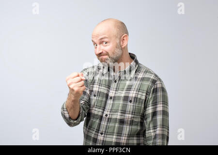 Reifen Mann mit Faust auf Kamera suchen mit Bedrohung auf grauem Hintergrund Bärtigen. Er täuscht sehr wütend zu sein Stockfoto