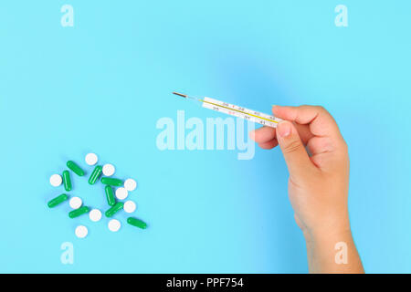 Ein Mann hält ein Thermometer in seine Hand mit einer hohen Temperatur vor einem blauen Tisch mit Tabletten. Top Anzeigen, Kopieren, flach Stockfoto