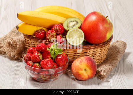 Frische Erdbeeren im Glas Schale gekrönt Minze, Nektarine, Kalk, Kiwi, Banane, Apfel in einem Weidenkorb auf einem Holztisch Stockfoto