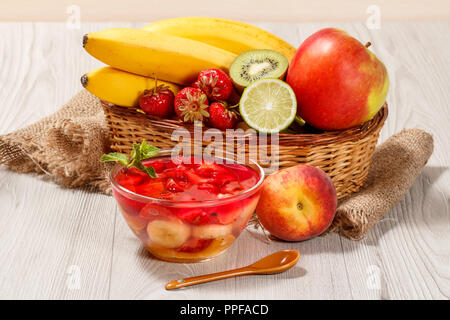 Cherry-Gelee mit Erdbeere Stücke in die Glasschale überstieg Minze, frische Erdbeeren, Nektarinen, Kalk, Kiwi, Banane, Apfel in einem Weidenkorb Stockfoto