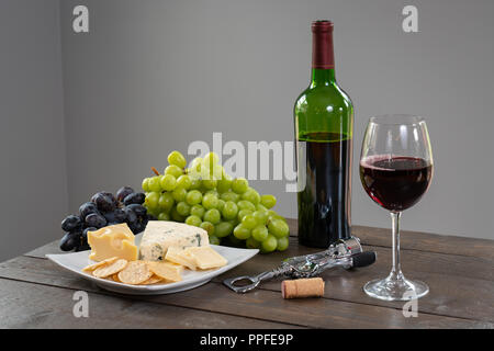 Glas Weißwein mit Flasche Wein, Käse und Trauben Stockfoto