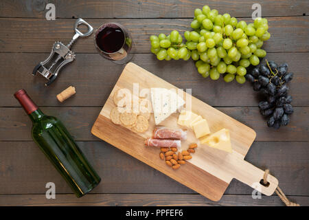 Glas Rotwein mit Flasche Wein, Käse, Cracker, Schinken, Mandeln und Trauben Stockfoto