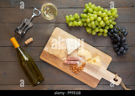 Glas Weißwein mit Flasche Wein, Käse, Cracker, Schinken, Mandeln und Trauben Stockfoto