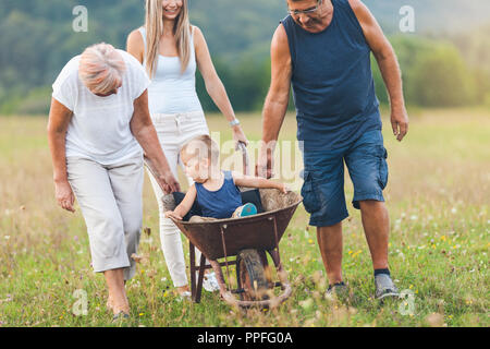 Familie drücken ihre kleinen Kinder und Enkel in einer Schubkarre Stockfoto