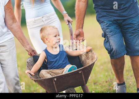 Familie drücken ihre kleinen Kinder und Enkel in einer Schubkarre Stockfoto