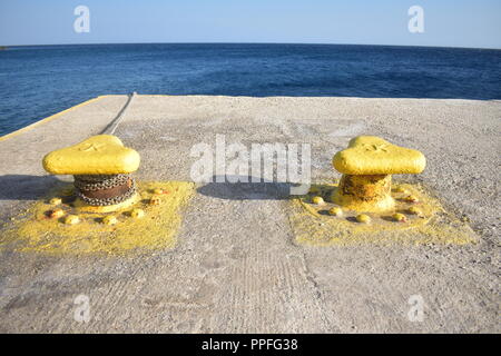 Griechenland, die charmante, abgelegene Insel Sikinos. Zwei gelb lackierte Poller am Dock der Bucht, am Rande des Meeres. Stockfoto