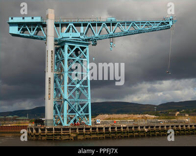 Gegen einen dunklen und grauer Himmel, ein Bungee Jumper hängt von der Ausleger des mächtigen Titan am Ufer des Flusses Clyde, Clydebank in der Nähe von Glasgow. Der Kran war einst Teil des berühmten John Brown Shipbuilding Yard und hat jetzt renoviert und ist ein beliebtes Reiseziel und Besucher, wo es einen atemberaubenden Blick von der Ausleger nach oben reisen der Lift dort zu erhalten. Stockfoto